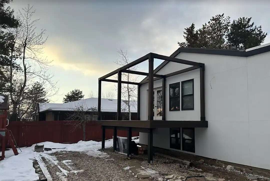 Photo of what it looks like to build a deck in winter. The deck frame is attached to the back of the house and snow covers the ground.