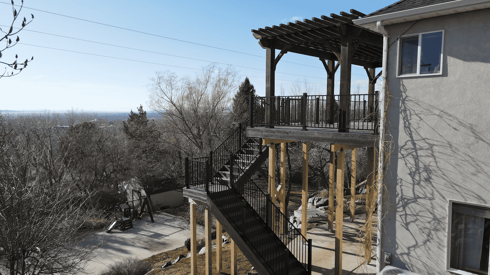 photo of an elevated deck with patio below, steps leading down, and pergola on the deck