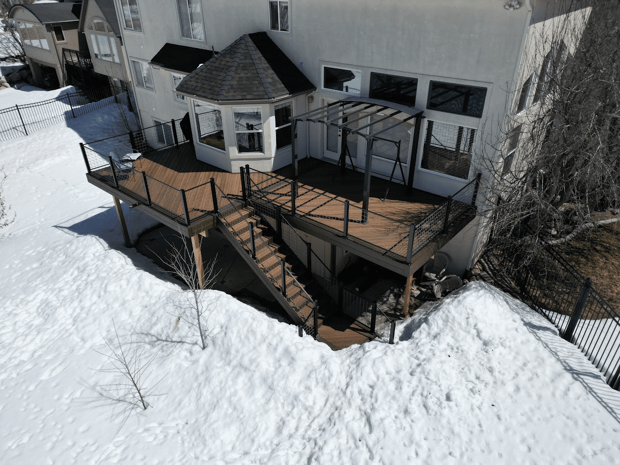 photo that captures the essence of build a deck in winter. Snow surrounds the elevated deck that includes a pergola, cable railing, and deck steps